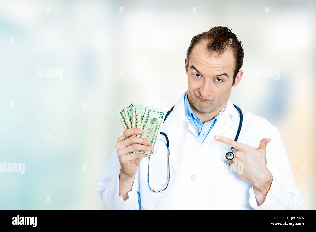 Healthcare financial system concept. Greedy miserly health care professional, male doctor holding money dollar bills standing in hospital clinic hallw Stock Photo