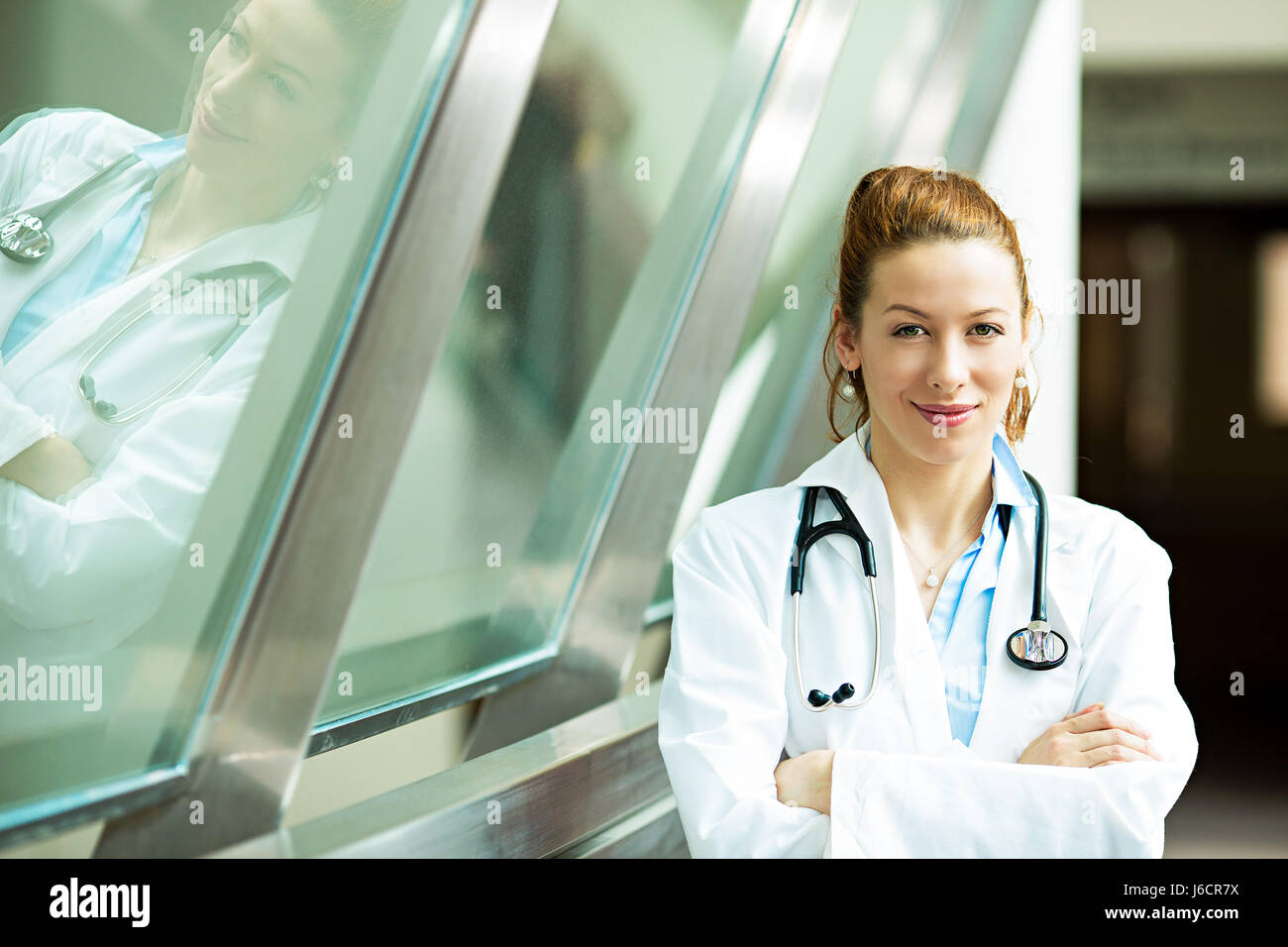 Closeup portrait young, smiling, confident, female doctor, healthcare professional with stethoscope standing, looking at you isolated background hospi Stock Photo