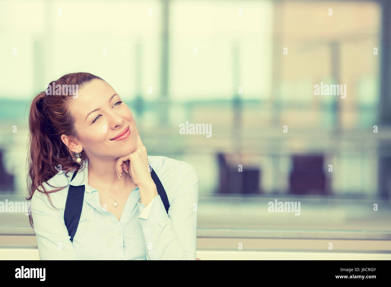 Portrait happy young woman thinking dreaming has many ideas looking up isolated office windows background. Positive human face expression emotion feel Stock Photo