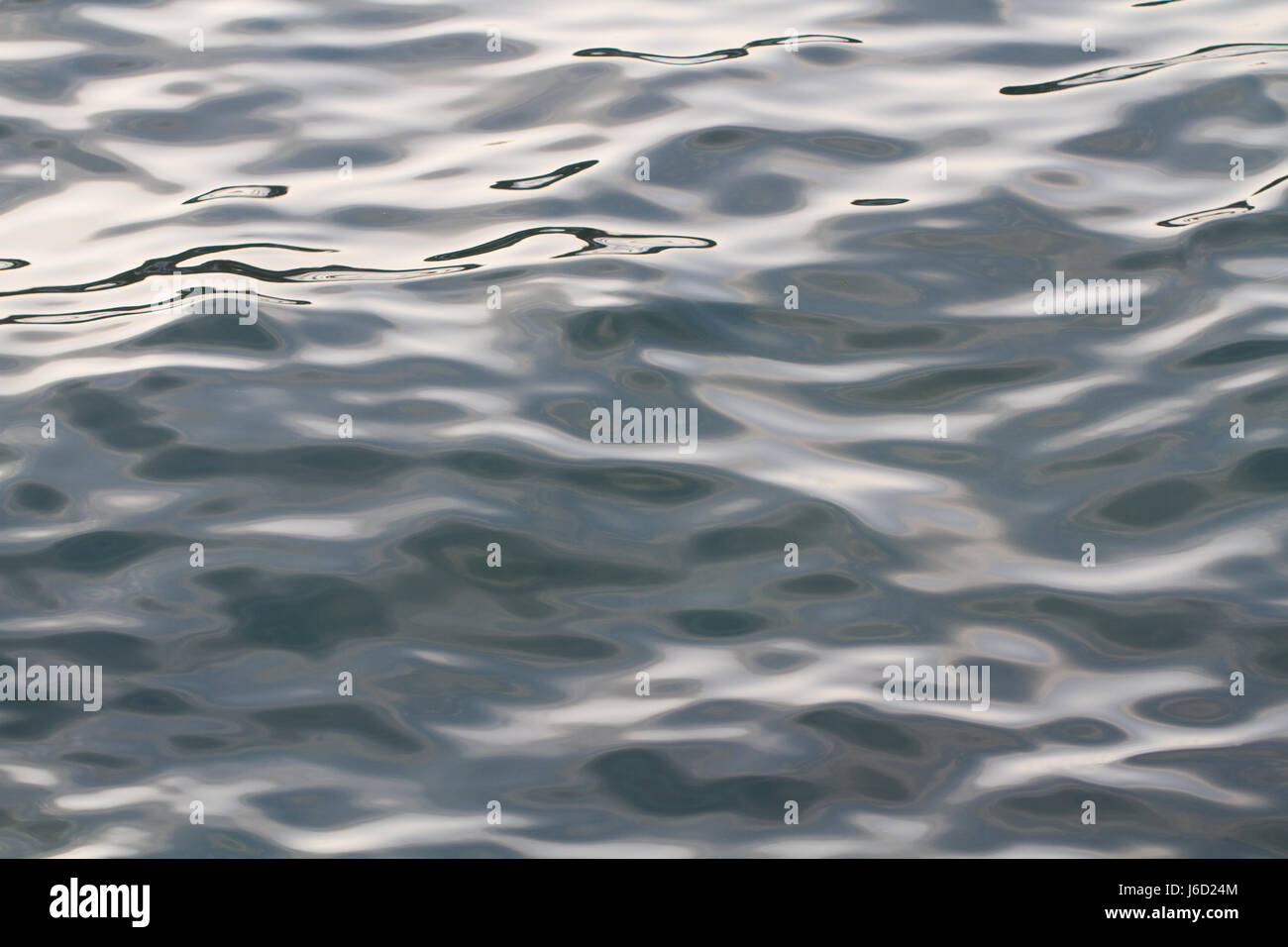 The surface of a cold, grey ocean with smooth ripples and waves that are contrasting between dark and light in a full frame nature background image.. Stock Photo
