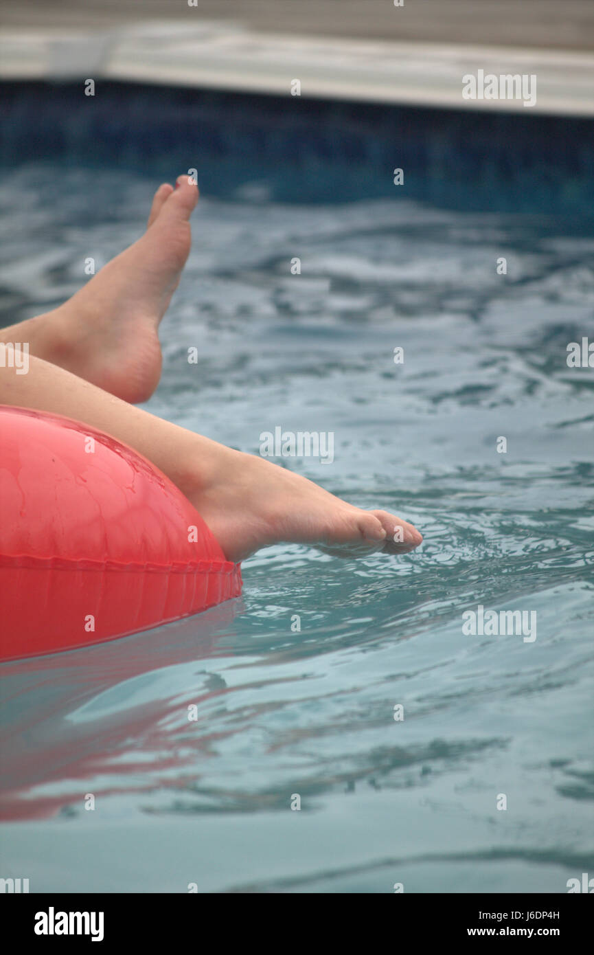Close up of child’s feet hanging off a red inner tube float in a pool