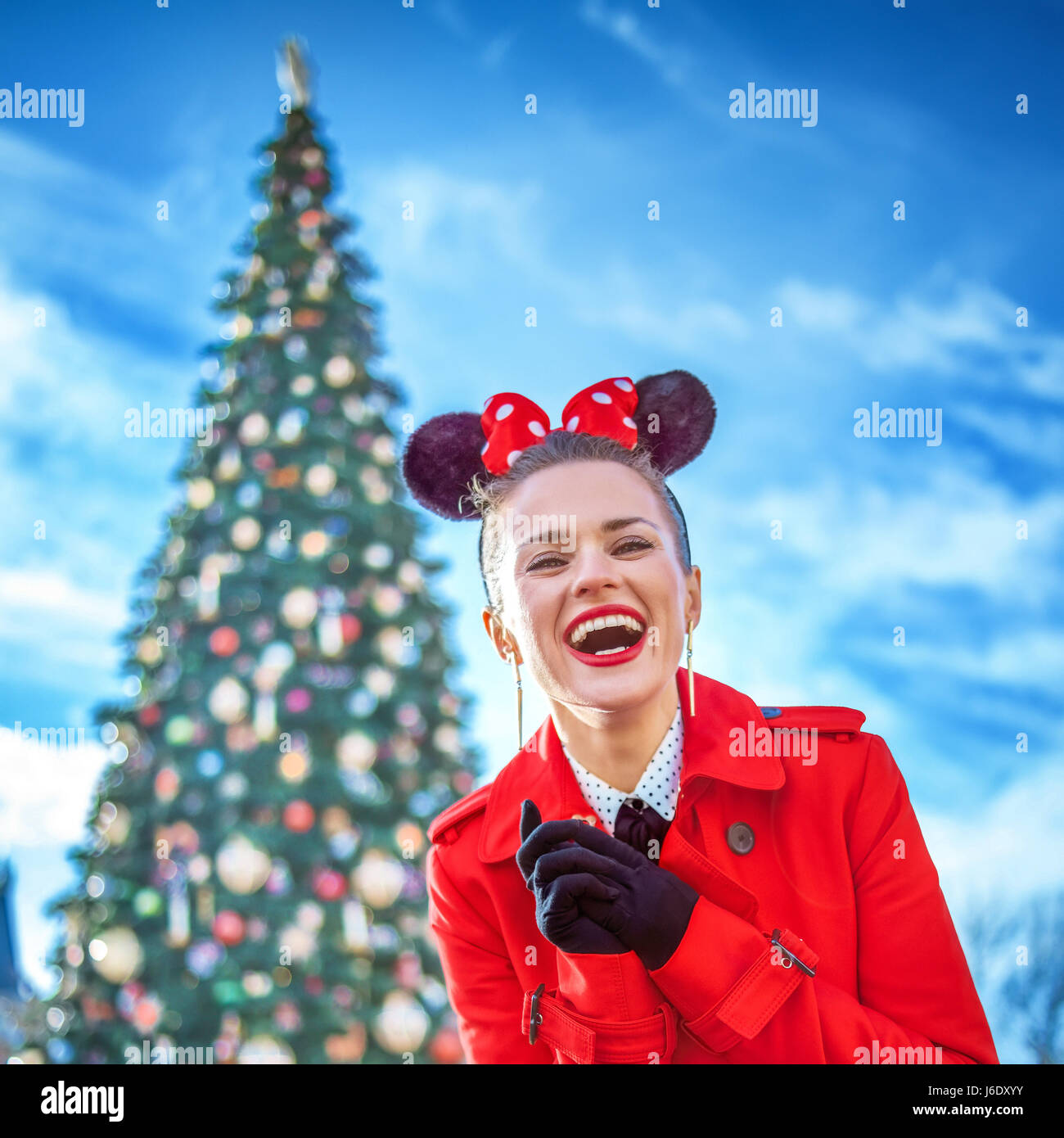 DISNEYLAND, FRANCE - DECEMBER, 8, 2016: smiling stylish woman in red trench coat in the front of big Christmas tree Stock Photo