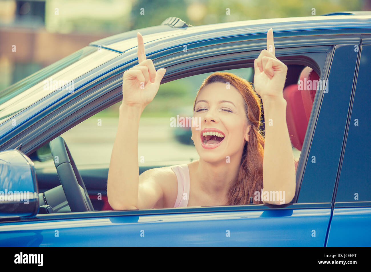 Side door view woman driver happy smiling showing thumbs up sitting inside new blue car  outside on parking lot background. Beautiful young woman happ Stock Photo