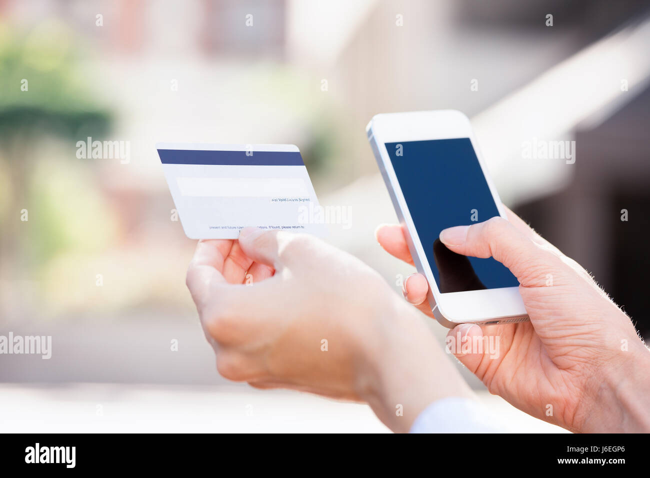 Closeup young woman hands holding credit card and using cell, smart phone for online shopping or reporting lost card, fraudulent transaction, isolated Stock Photo