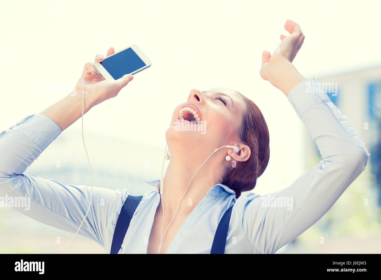 Beautiful happy smiling woman listening to music with earphones looking arms raised up in the sky. Positive face expression, emotion, feeling. Fun, le Stock Photo