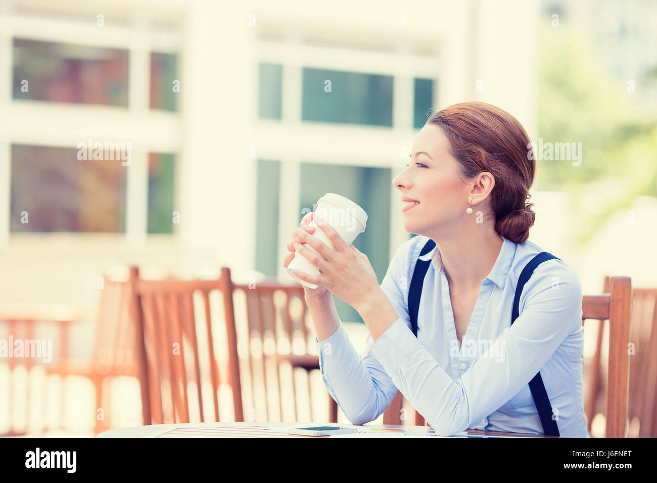Side profile portrait woman drinking coffee in sun sitting outdoor in sunshine light enjoying her morning tea. Smiling happy businesswoman model in he Stock Photo