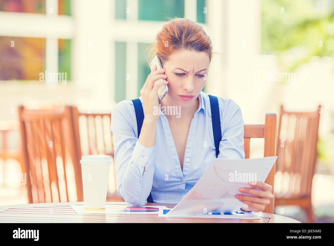 Closeup portrait upset sad, skeptical, unhappy, serious woman talking on phone holding looking at documents outside corporate office background. Negat Stock Photo