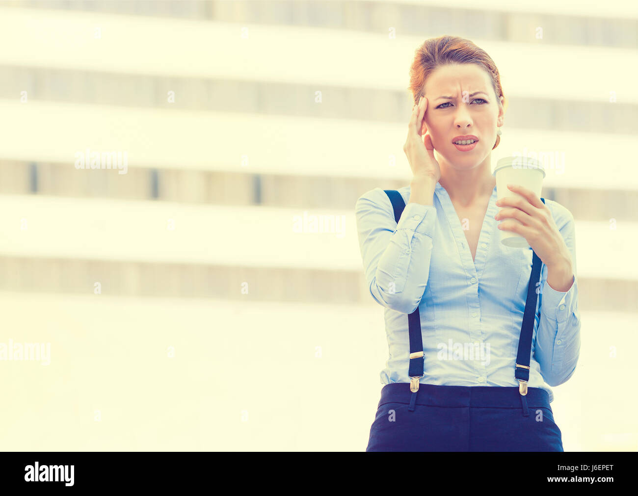 Portrait stressed worried young woman holding cup of coffee. Corporate employee having headache isolated outdoors corporate office window building bac Stock Photo