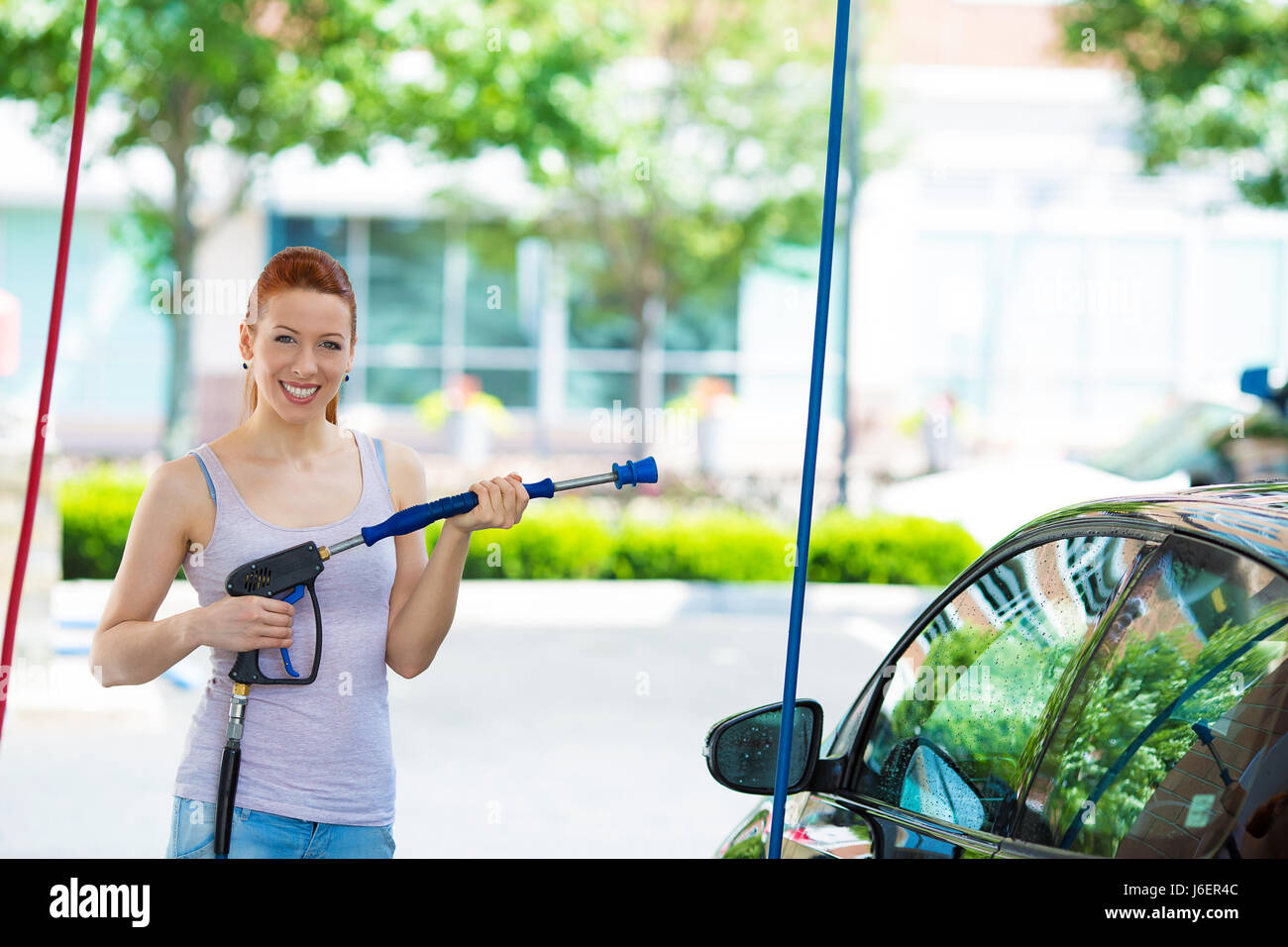 Picture, portrait young, smiling, happy, attractive woman washing automobile at manual car washing self service station, cleaning with foam, pressured Stock Photo