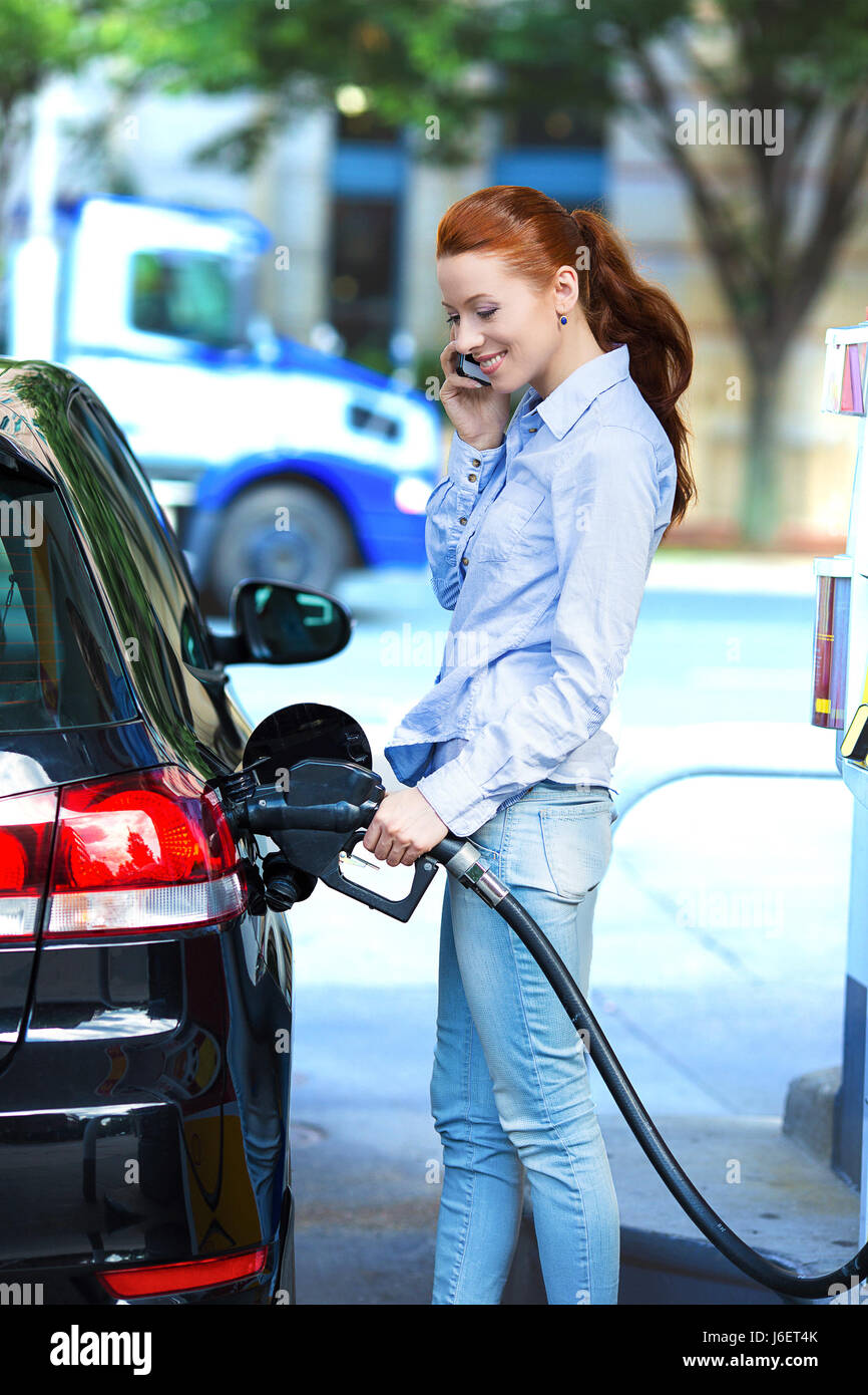 Portrait happy smiling pretty, attractive woman filling compact car tank with petrol at gas station isolated city background. Oil prices economy, ener Stock Photo