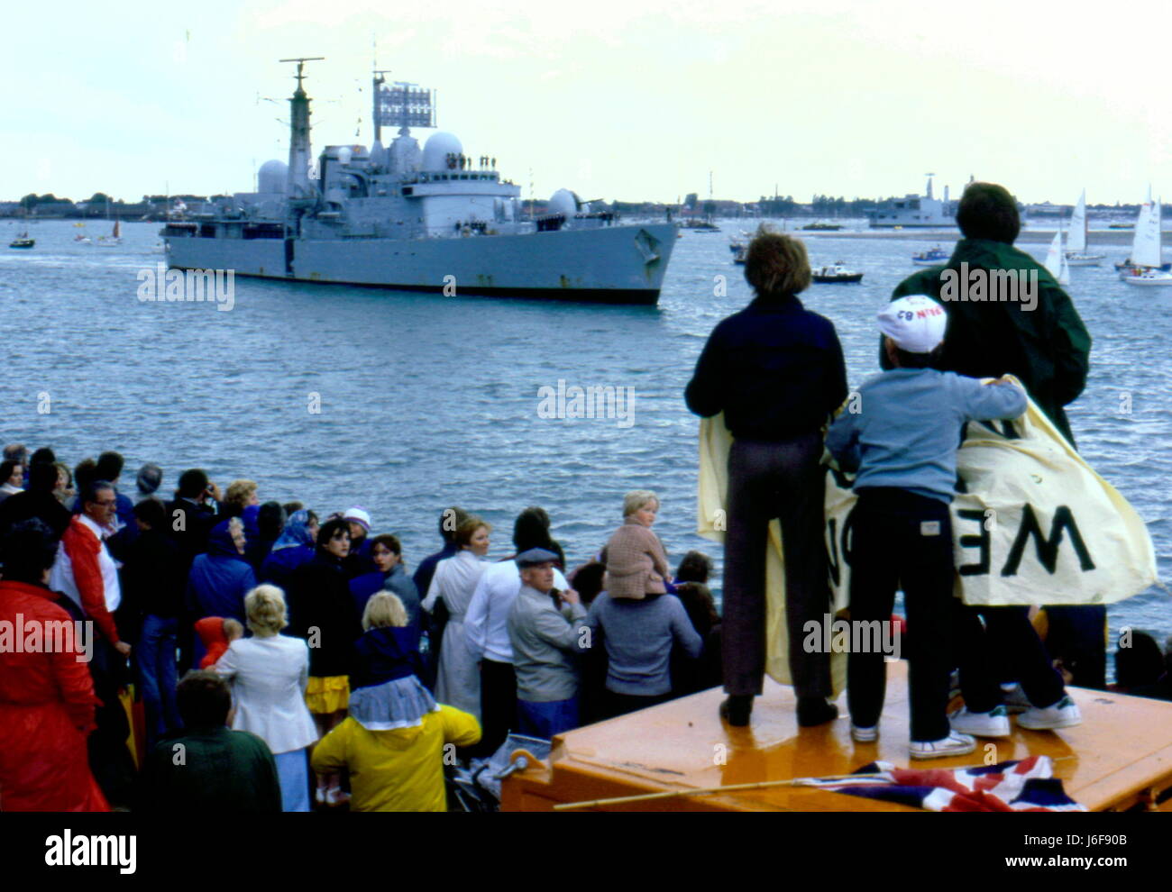 AJAXNETPHOTO. 19TH JUNE. 1982. PORTSMOUTH, ENGLAND. - SURVIVOR RETURNS - THE TYPE 42 (1&2) SHEFFIELD CLASS DESTROYER (3660 TONS) HMS GLASGOW, A PATCH IN HER HULL VISIBLE WHERE AN ARGENTINE BOMB ENTERED THE HULL, RETURNS HOME TO CROWDS OF WELL-WISHERS GATHERED ON FOUNTAIN LAKE JETTY.  PHOTO:JONATHAN EASTLAND/AJAX. REF:910168 Stock Photo