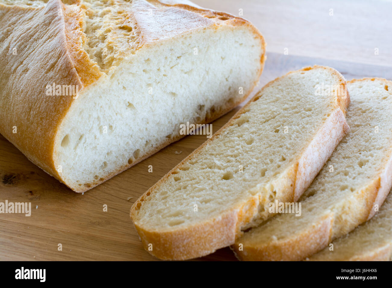 Slices and loaf of bread on wooden oak table top. Shallow depth of ...