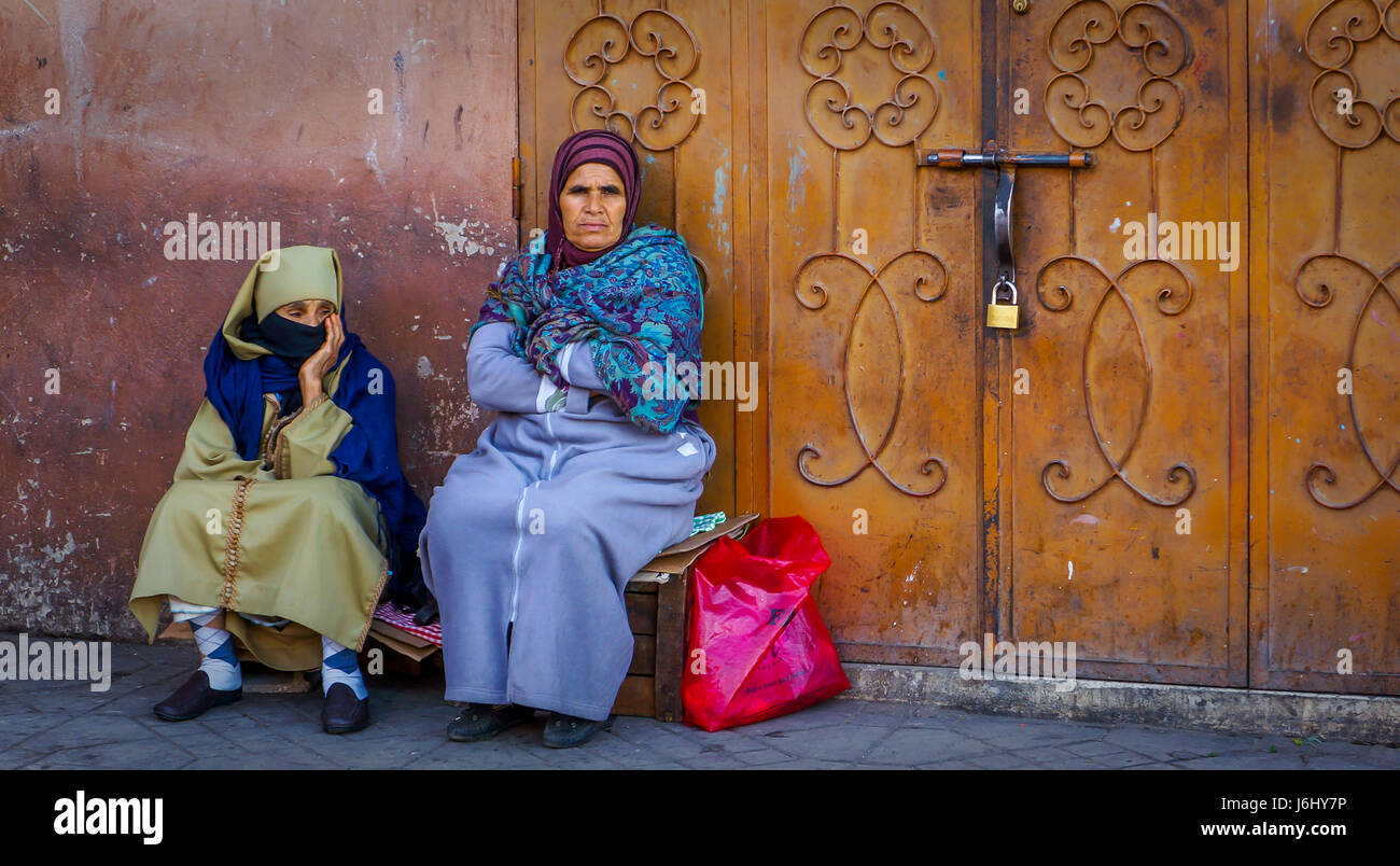 Two women sitting outside locked door in Marrakech, Morocco Stock Photo
