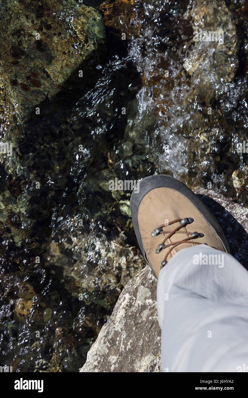 Hiker wade a rocky mountain stream with very used trekking boots. Concept of high reliability Stock Photo