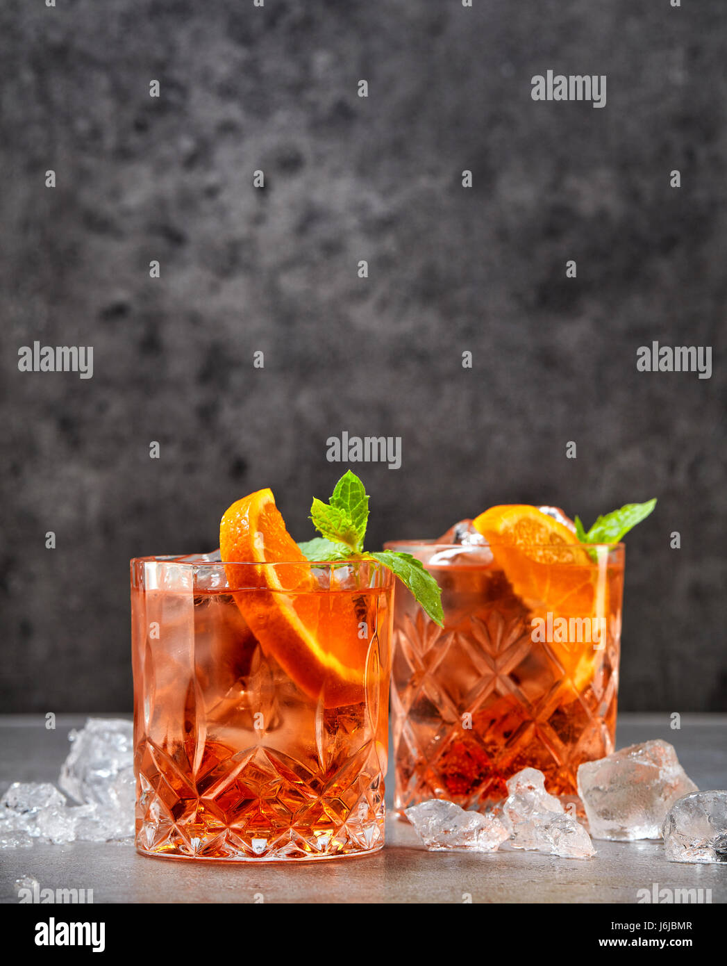 two glasses of aperol soda cocktail and ice cubes on grey table Stock Photo