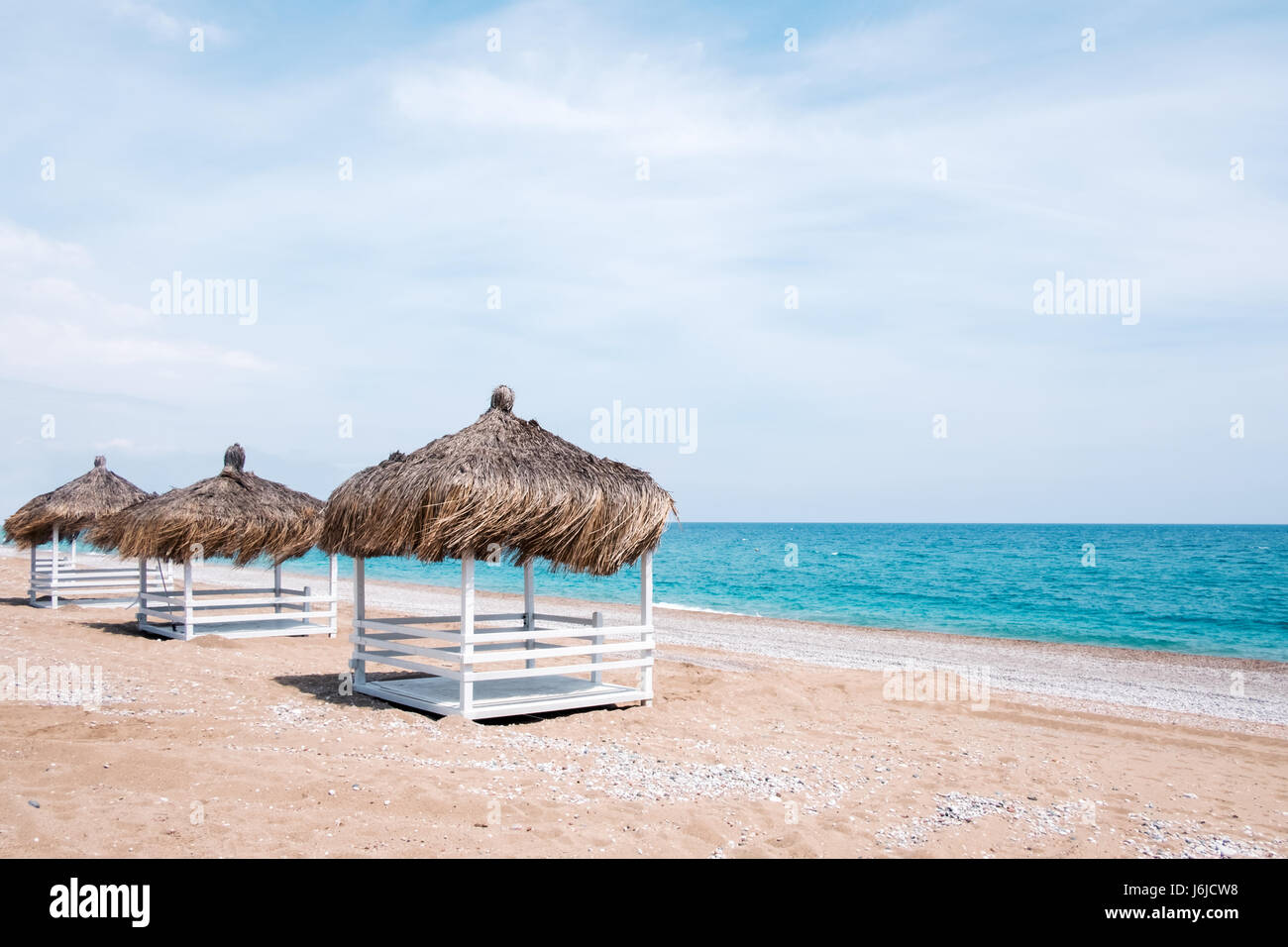 Summer arbors on beach. Breathtaking view on mediterranean sea. White wooden summerhouses on sunny day. Blue sky and fluffy clouds Stock Photo