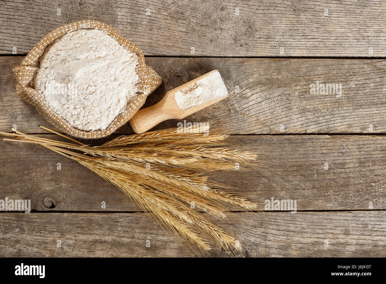 wholegrain flour in burlap bag and wheat ears on wooden table. Top view. Copy space. Baking background. Flour Stock Photo