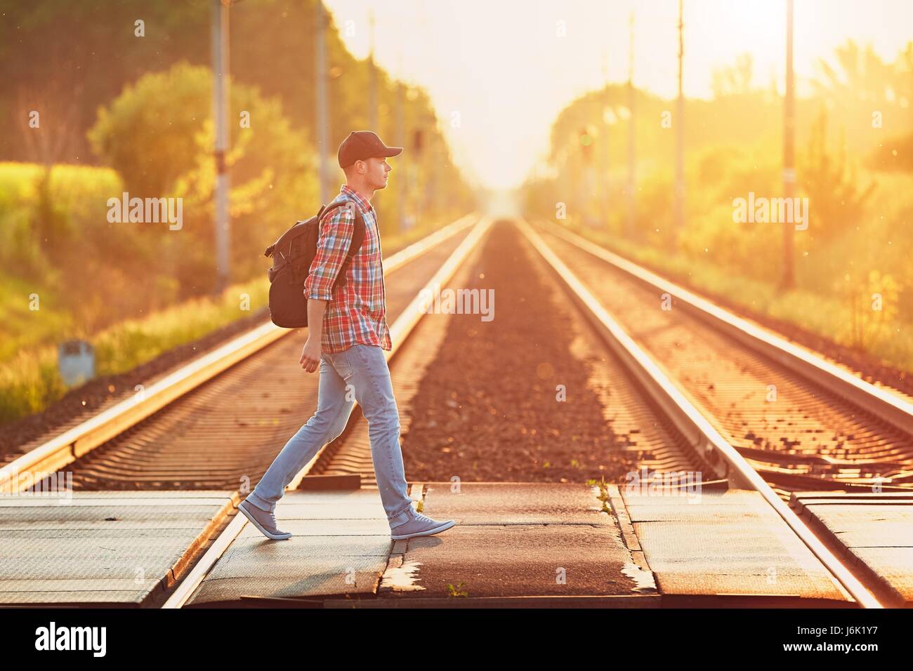 Traveling by train to nature. Young man with backpack and cap enjoying from trip during sunset (golden hour). Stock Photo