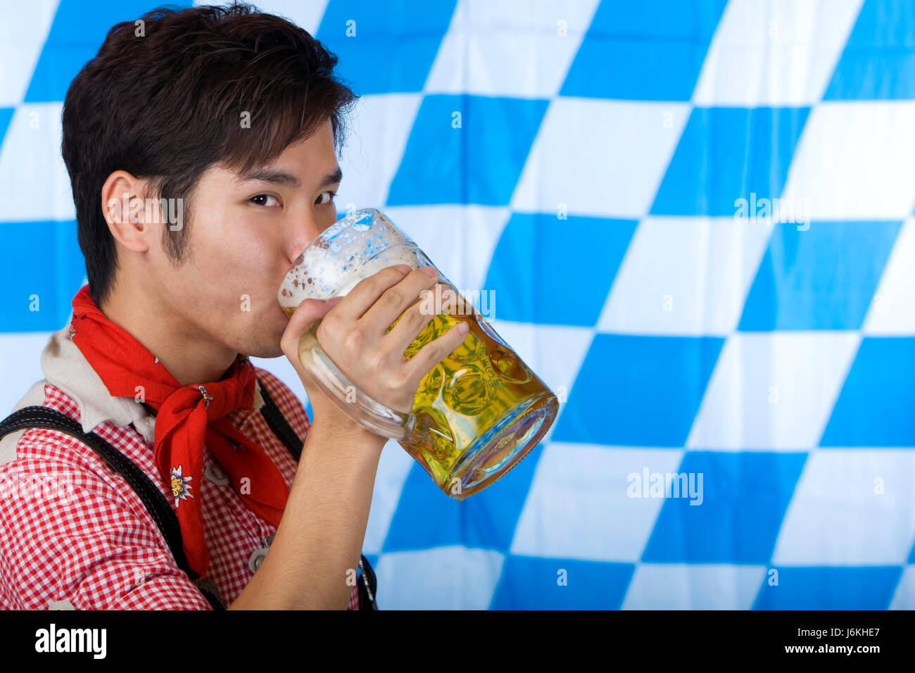 chinese man in lederhosen drinking beer out of oktoberfest beer stein Stock Photo