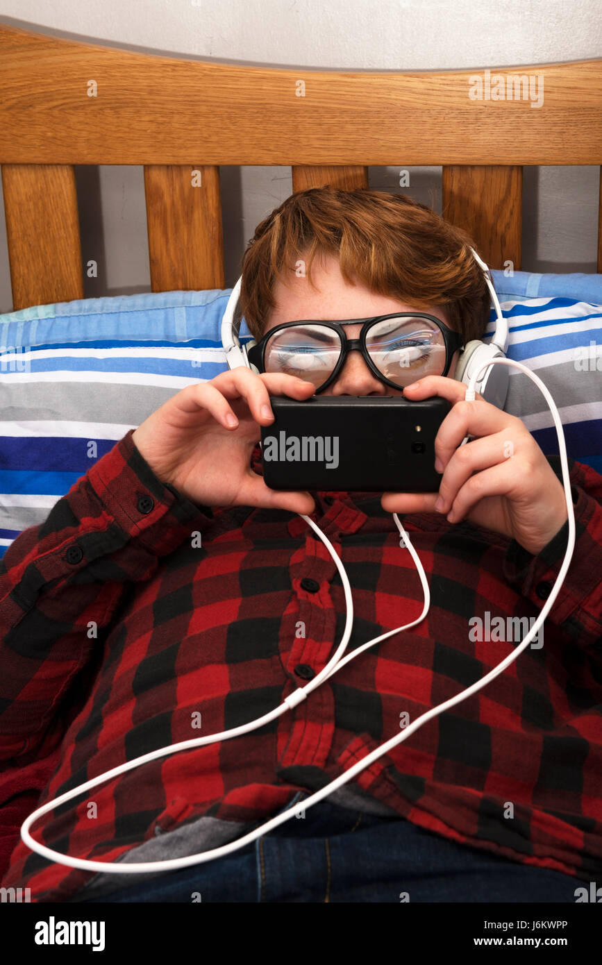 11-year old boy in bedroom using a smart phone to access the internet Stock Photo
