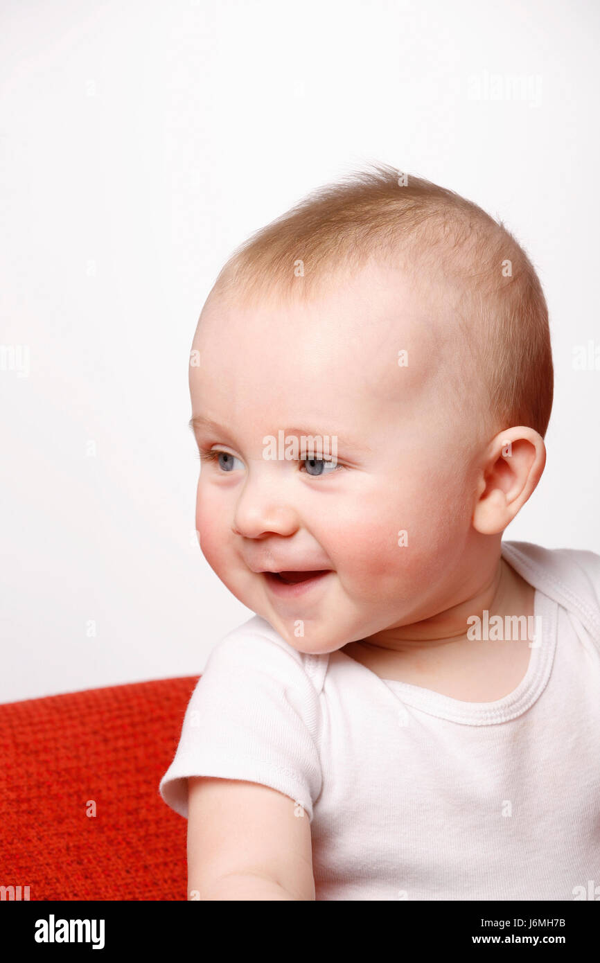 Happy six month old baby boy sitting on a red sofa, making facial expressions. Stock Photo