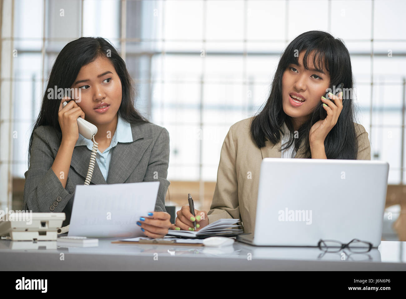 two businesswomen communicating with their clients on the phone Stock Photo