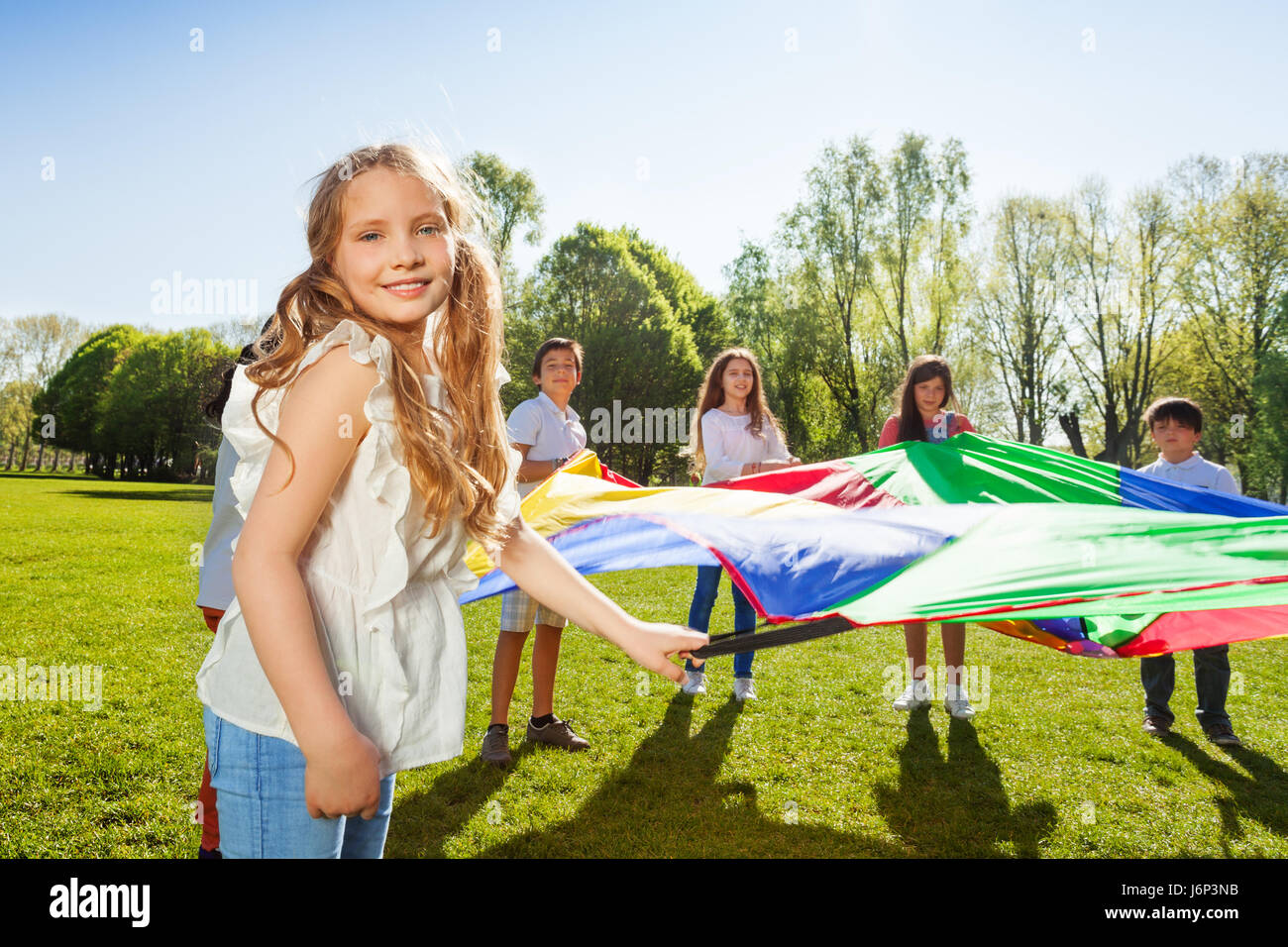 Portrait of lovely blonde girl waving rainbow parachute standing ...