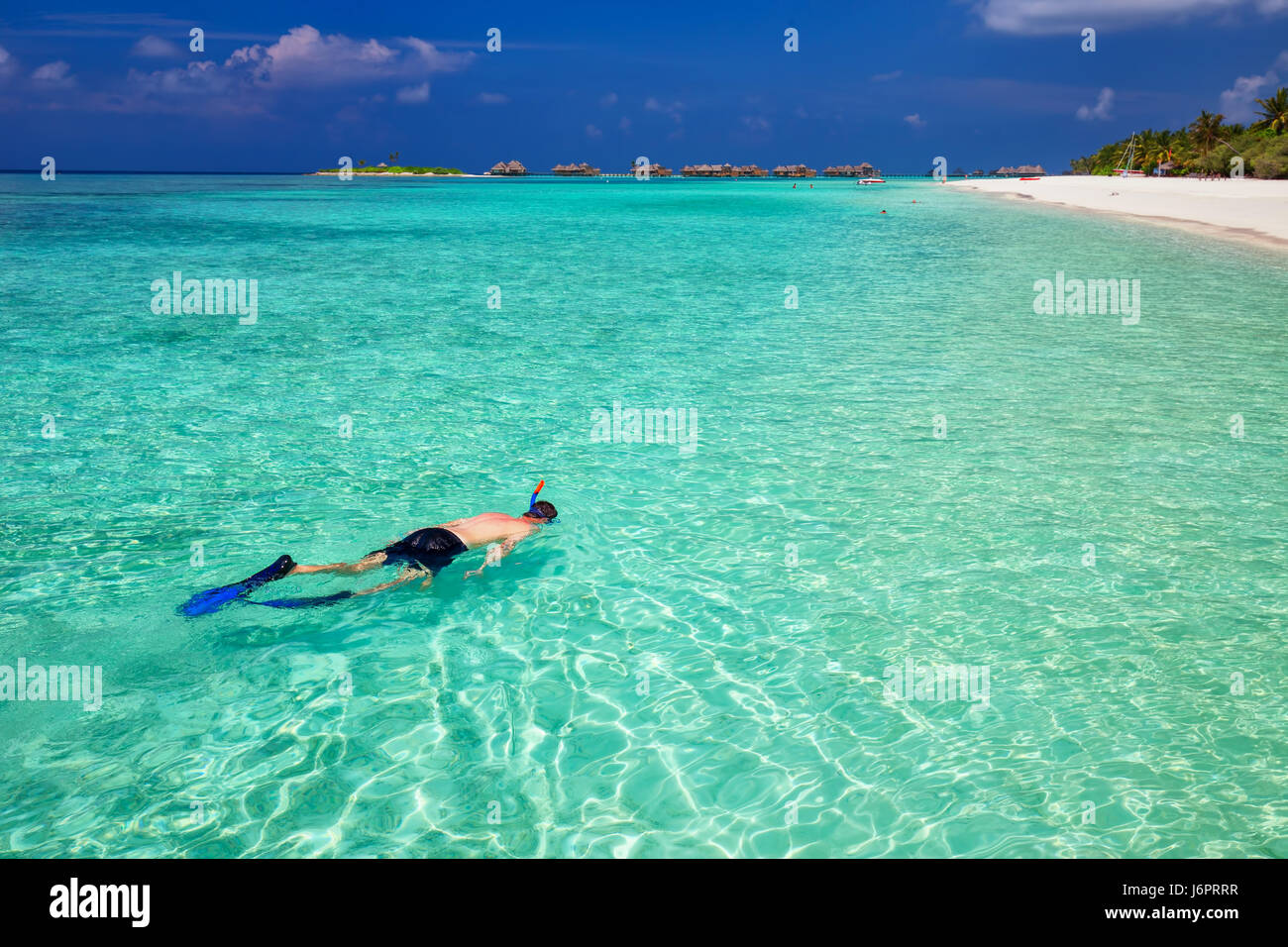 Young man snorkling in tropical lagoon with over water bungalows, Maldives Stock Photo