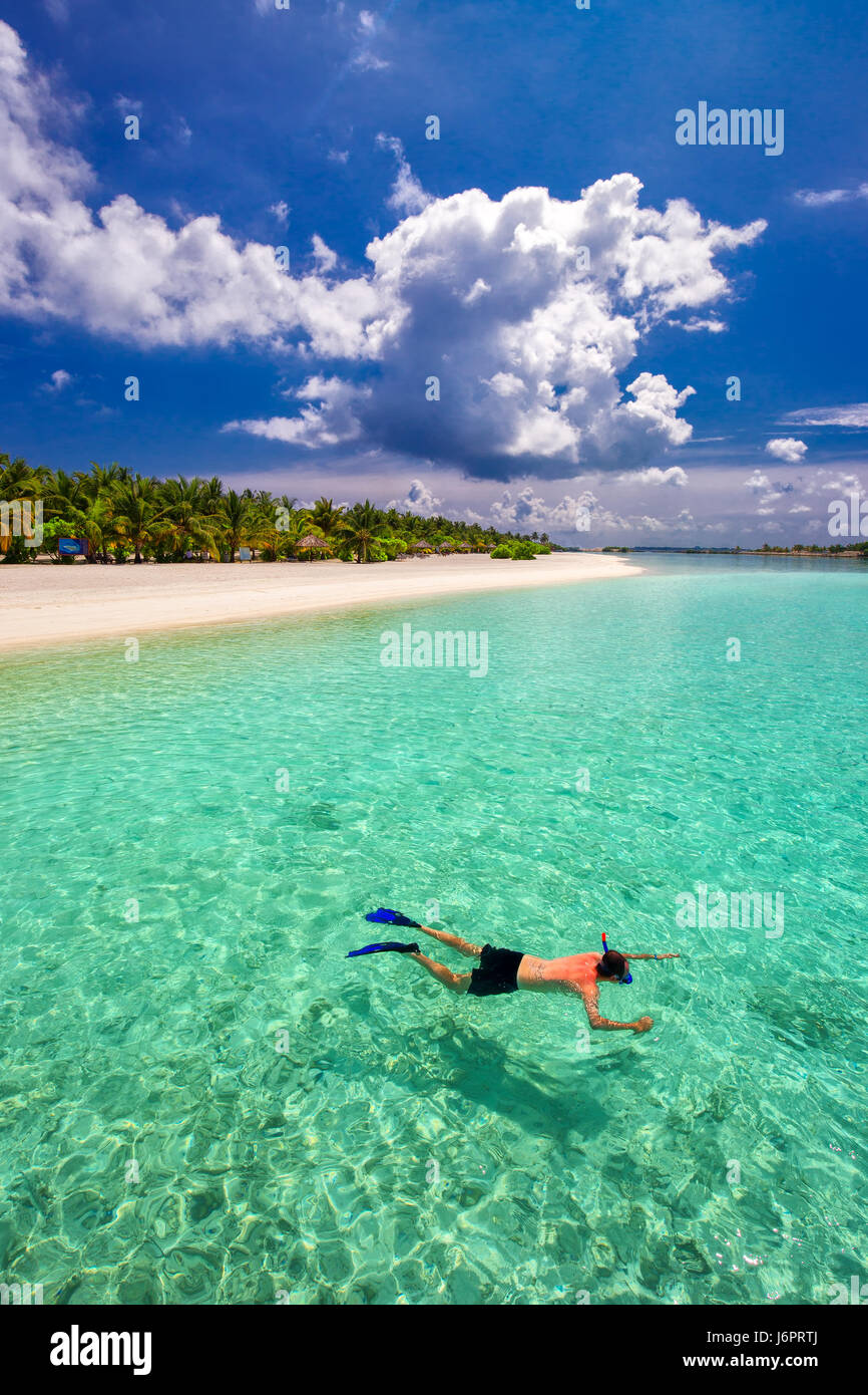 Young man snorkling in tropical lagoon with over water bungalows, Maldives Stock Photo