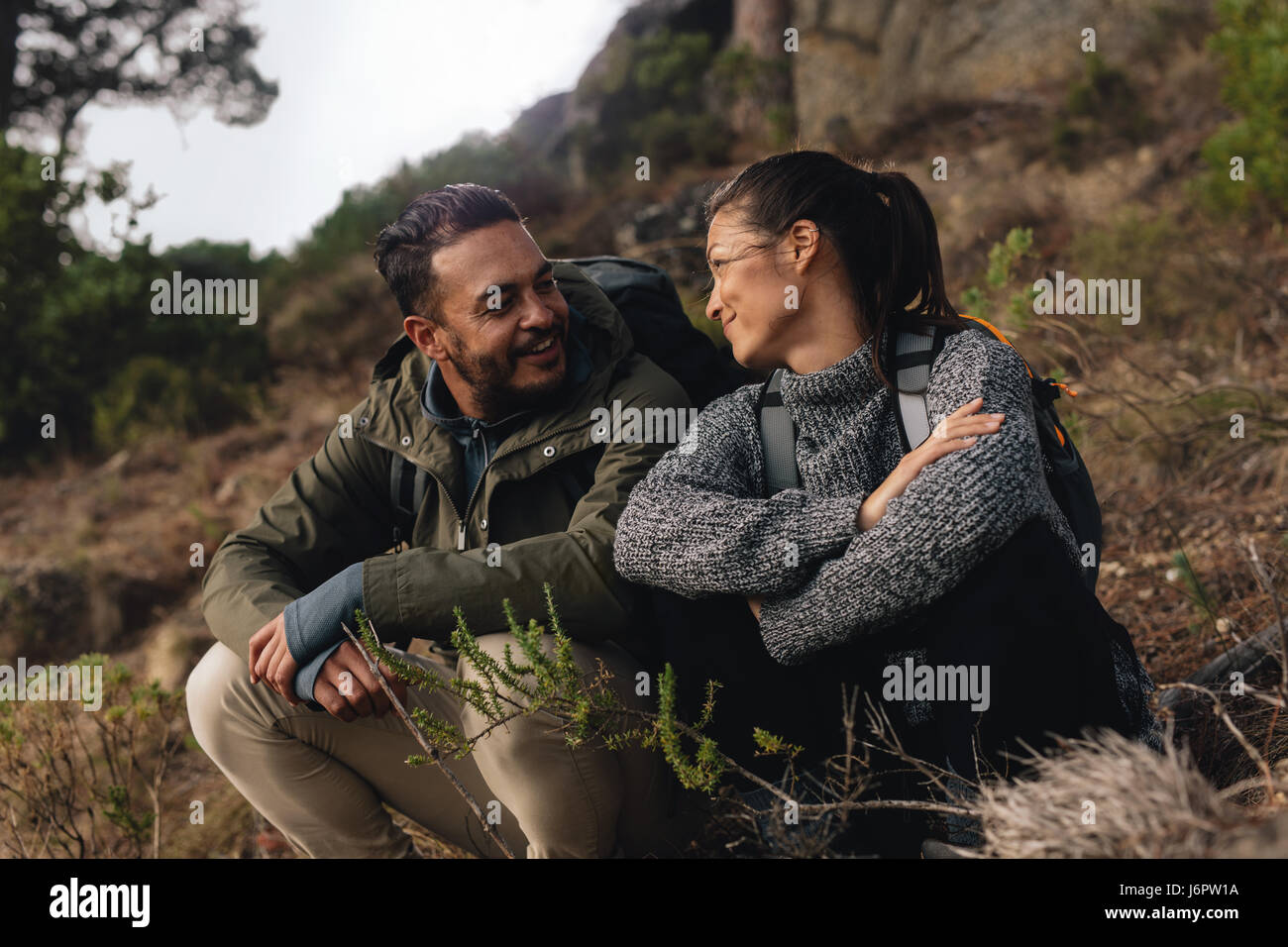 Young couple taking a break on a hike. Man and woman sitting and taking rest during hiking. Stock Photo