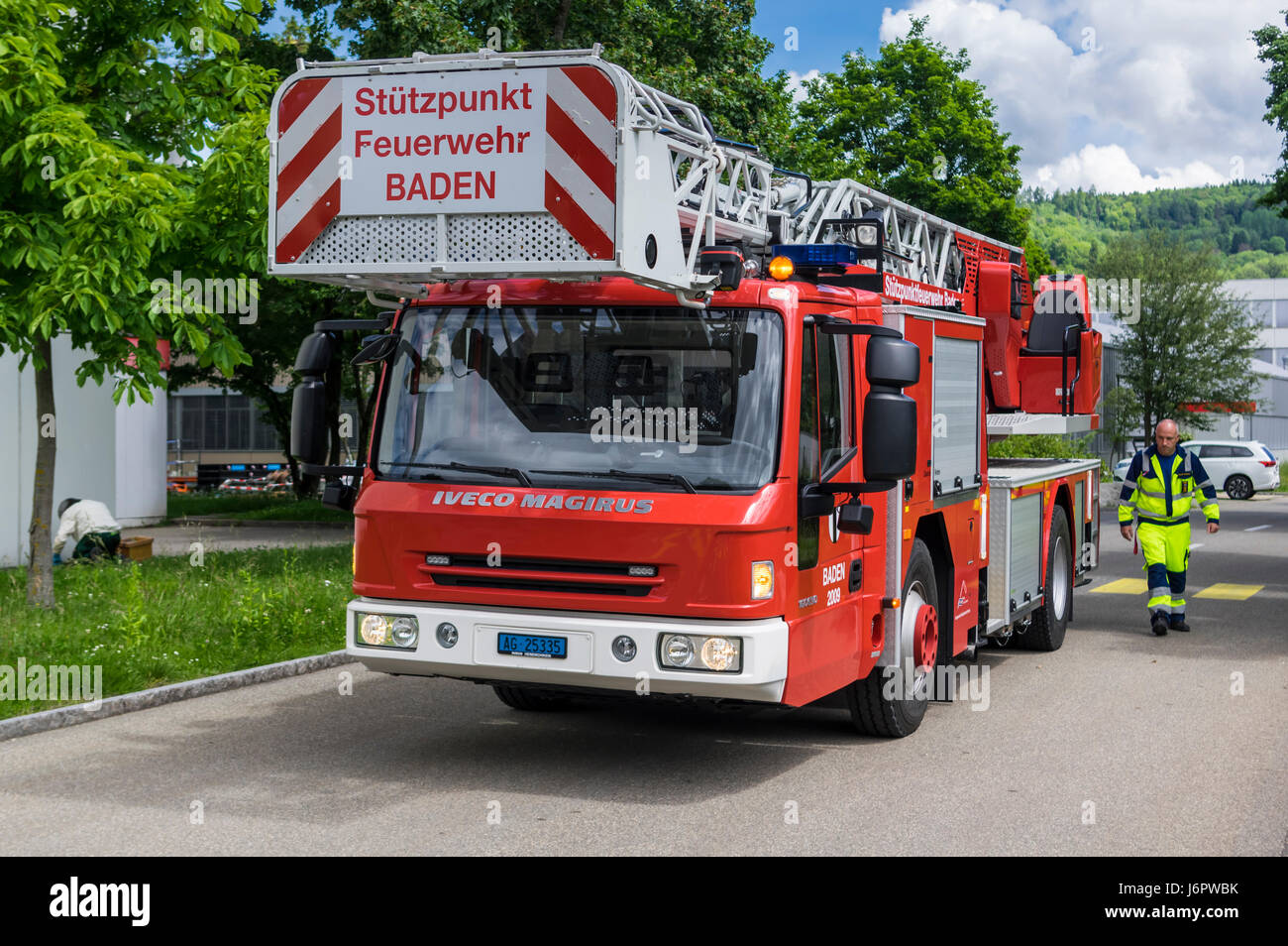 Iveco Magirus 160E30 turntable ladder truck of a Swiss fire brigade. Ladder and platform retracted. Fireman standing next to the vehicle. Stock Photo