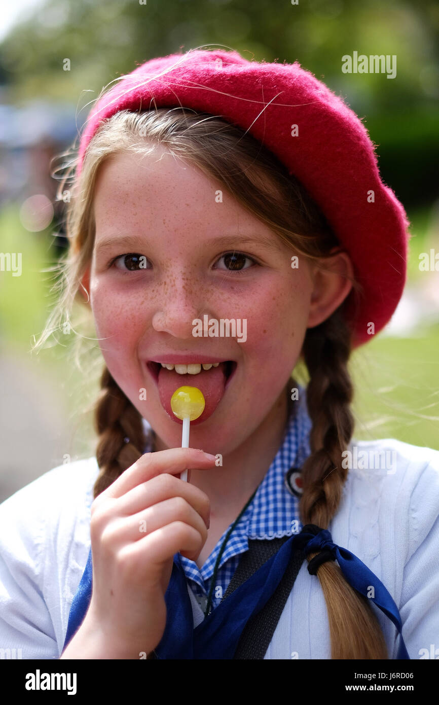 Young girl in school uniform and red beret licks a yellow lollypop Stock Photo