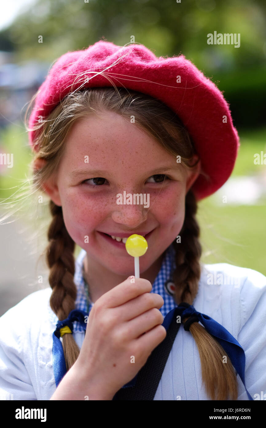 Young girl in school uniform and red beret licks a yellow lollypop Stock Photo