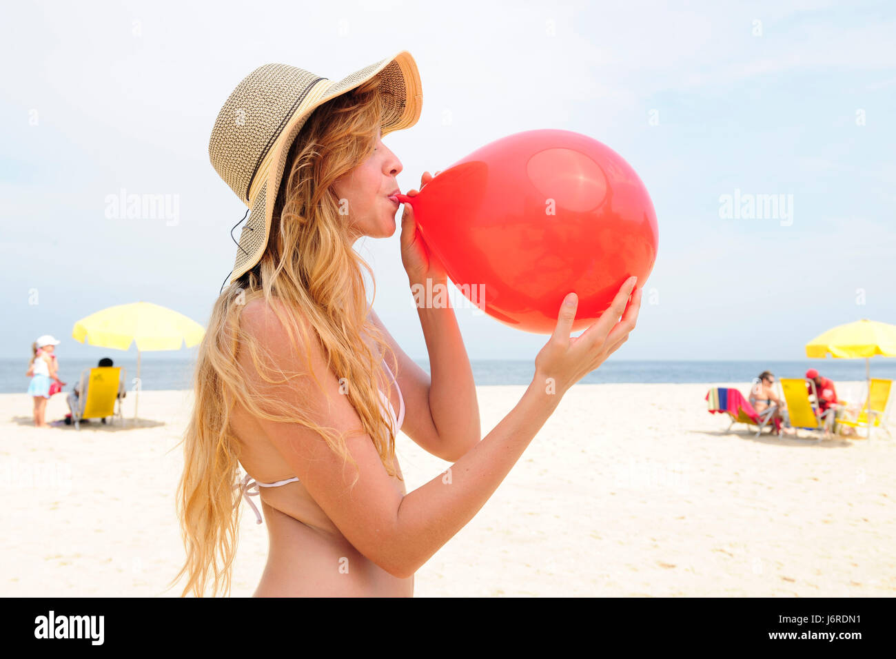 Девушка надувает шар. Пляж надувают матрас. Шарики на пляже. Женщина надувает шар. Шар на пляже.