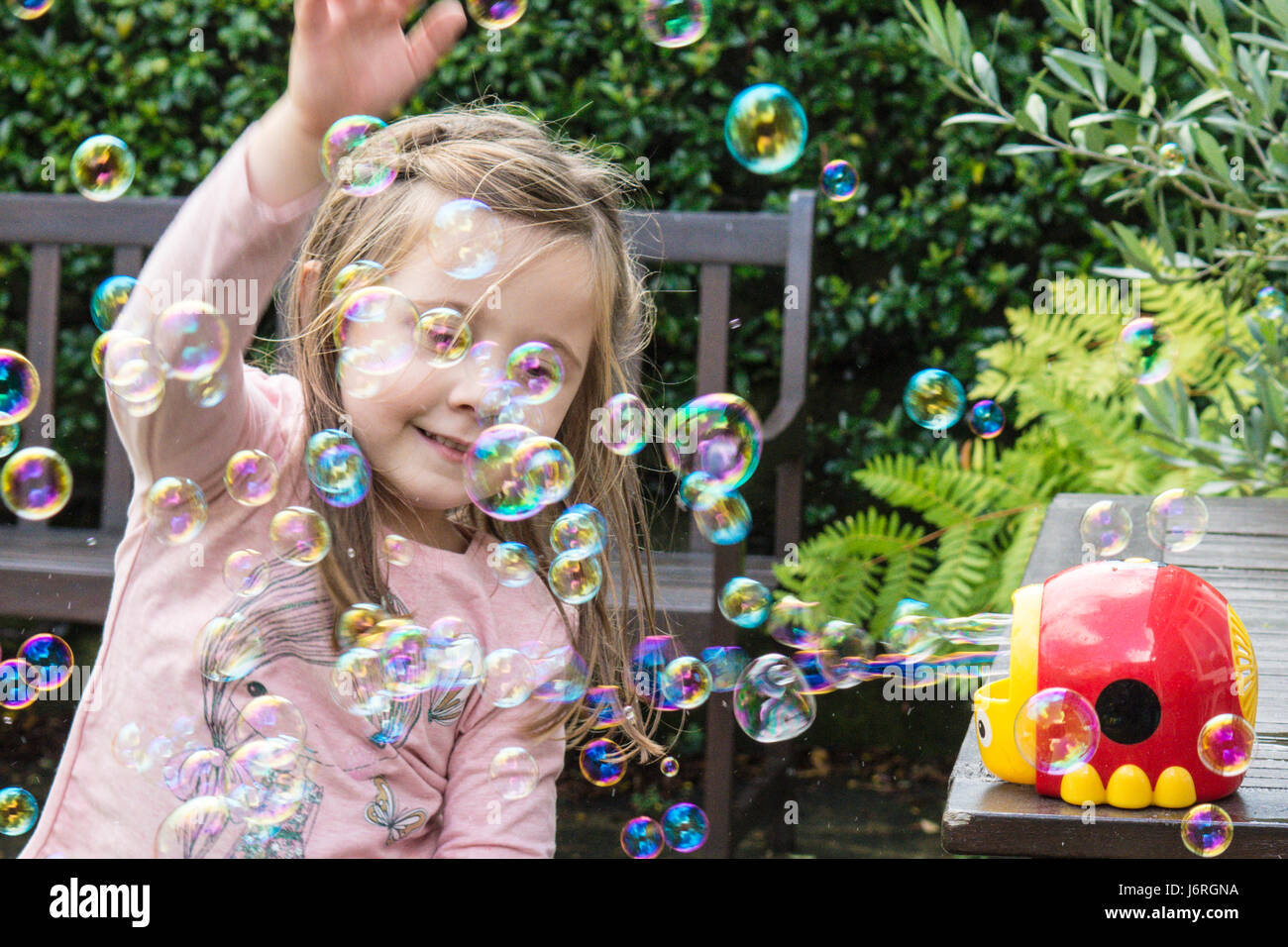three year old girl playing in bubbles made by a bubble machine in a garden. Sussex, UK. Stock Photo
