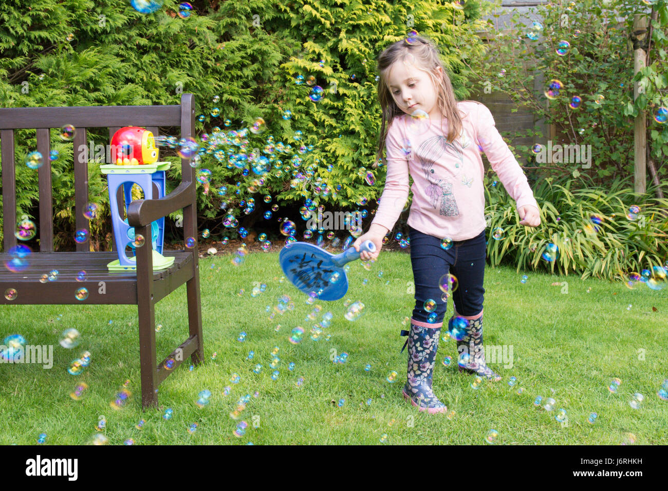 three year old girl hitting with a bat bubbles made by a bubble machine