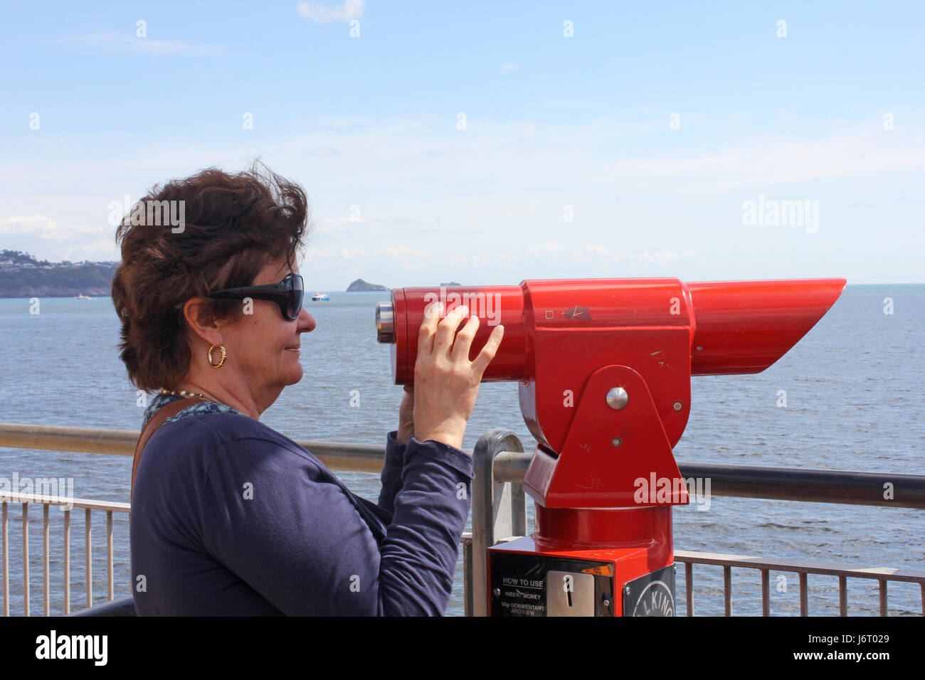 Woman looking through a coin operated telescope on a pier at the seaside in the UK Stock Photo