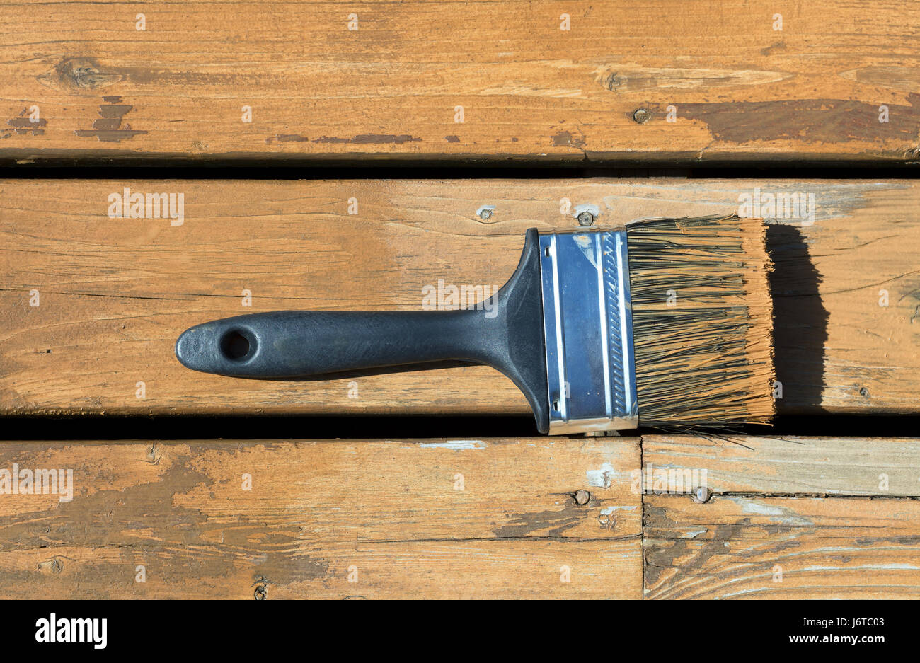 Used paintbrush filled with wood stain on a natural cedar wooden deck Stock Photo