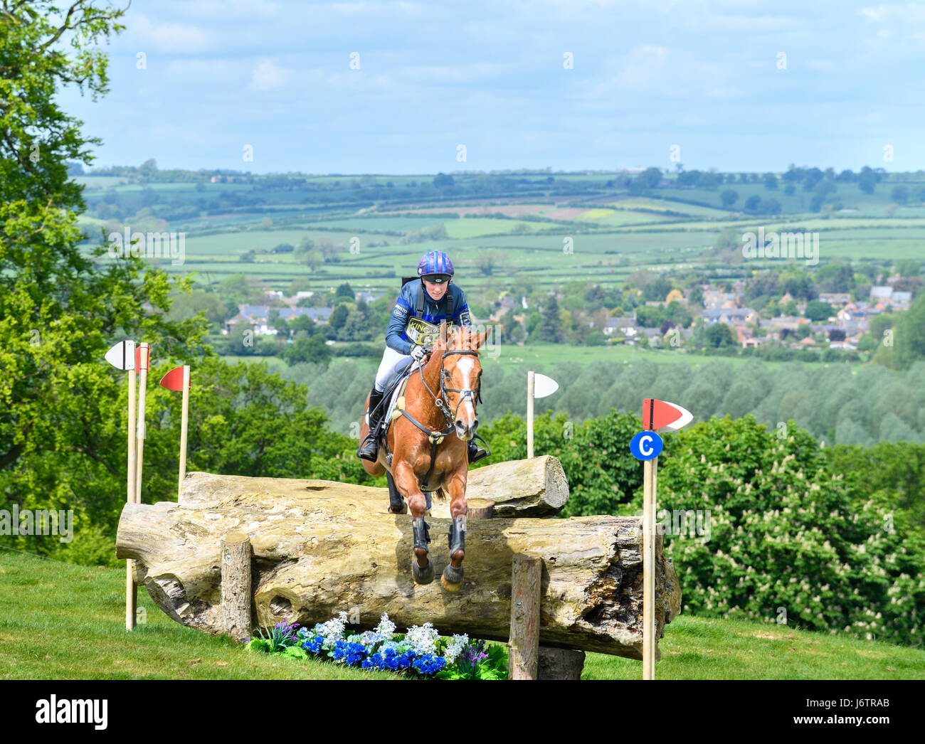 Rockingham Castle, Corby, UK. 21st May, 2017. Riding Drops of Brandy, Zara Tindall (granddaughter of Queen Elizabeth II of the United Kingdom) clears a tree trunk obstacle with the Welland valley in the background on a sunny day during the cross country phase of the Rockingham International Horse Trials in the grounds of the Norman castle at Rockingham, Corby, England on 21st May 2017. Credit: miscellany/Alamy Live News Stock Photo