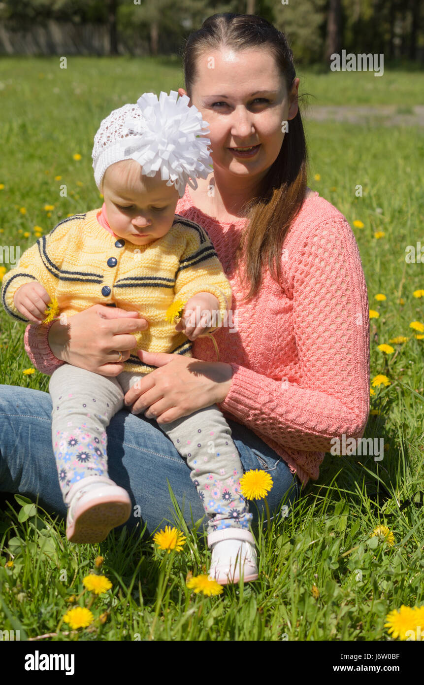 Mom and daughter sitting on green grass with yellow flowers. Stock Photo