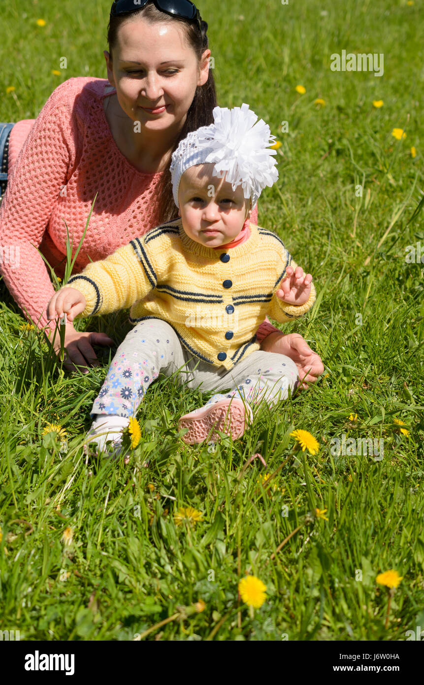 Mom and daughter sitting on green grass with yellow flowers. Stock Photo