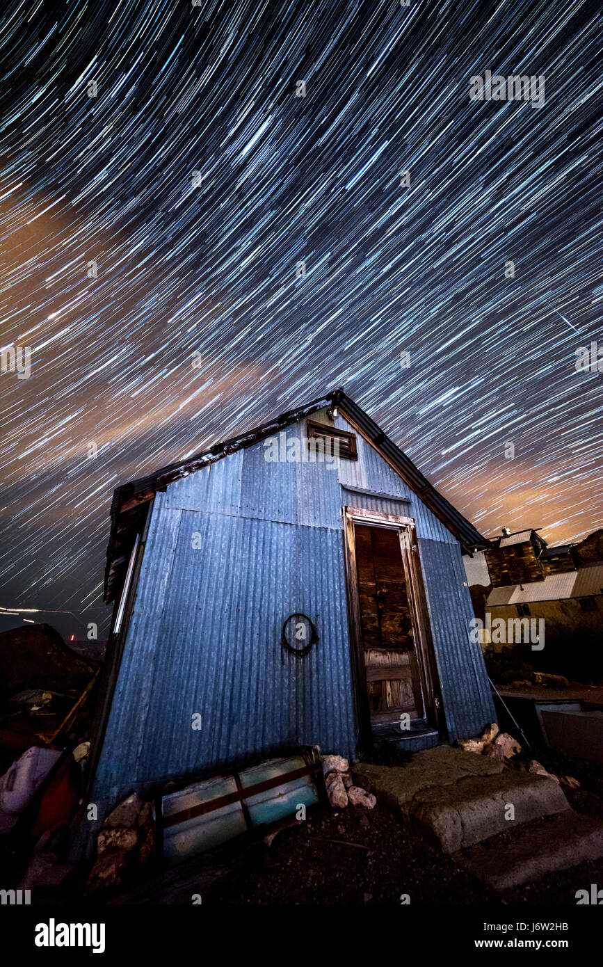 Star trail photography captures the path of distant stars framed against an old minimg shack as the earth rotates. Stock Photo