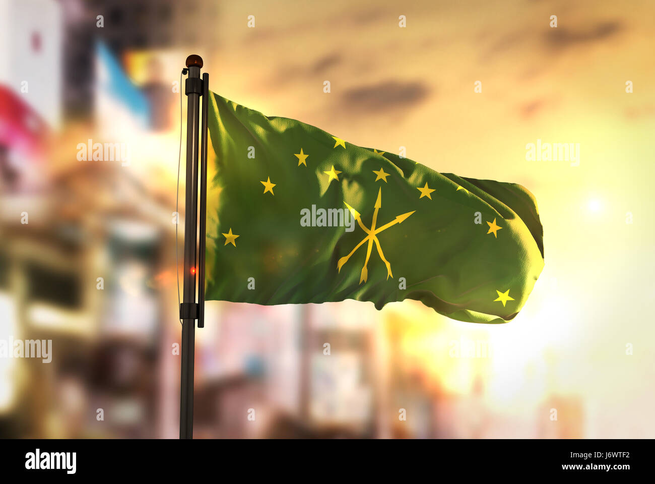 Adygea Flag Against City Blurred Background At Sunrise Backlight Stock Photo