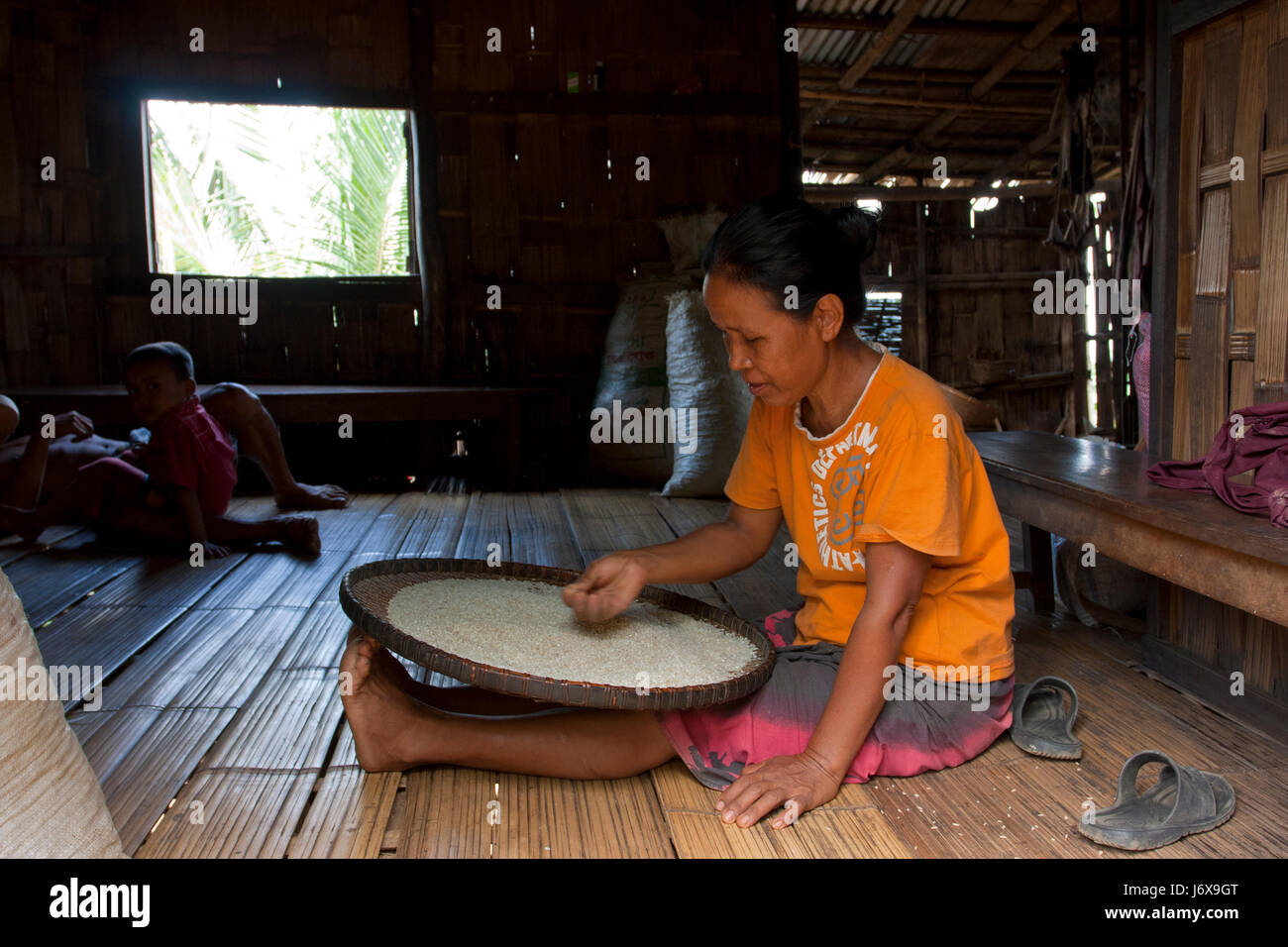 An ethnic woman sifting rice at her home. Khagrachari, Bangladesh. Stock Photo