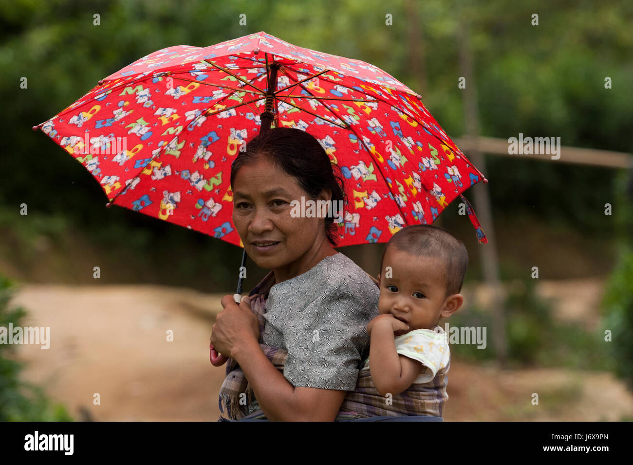 An ethnic mother carries her baby on her back. Khagrachari, Bangladesh. Stock Photo
