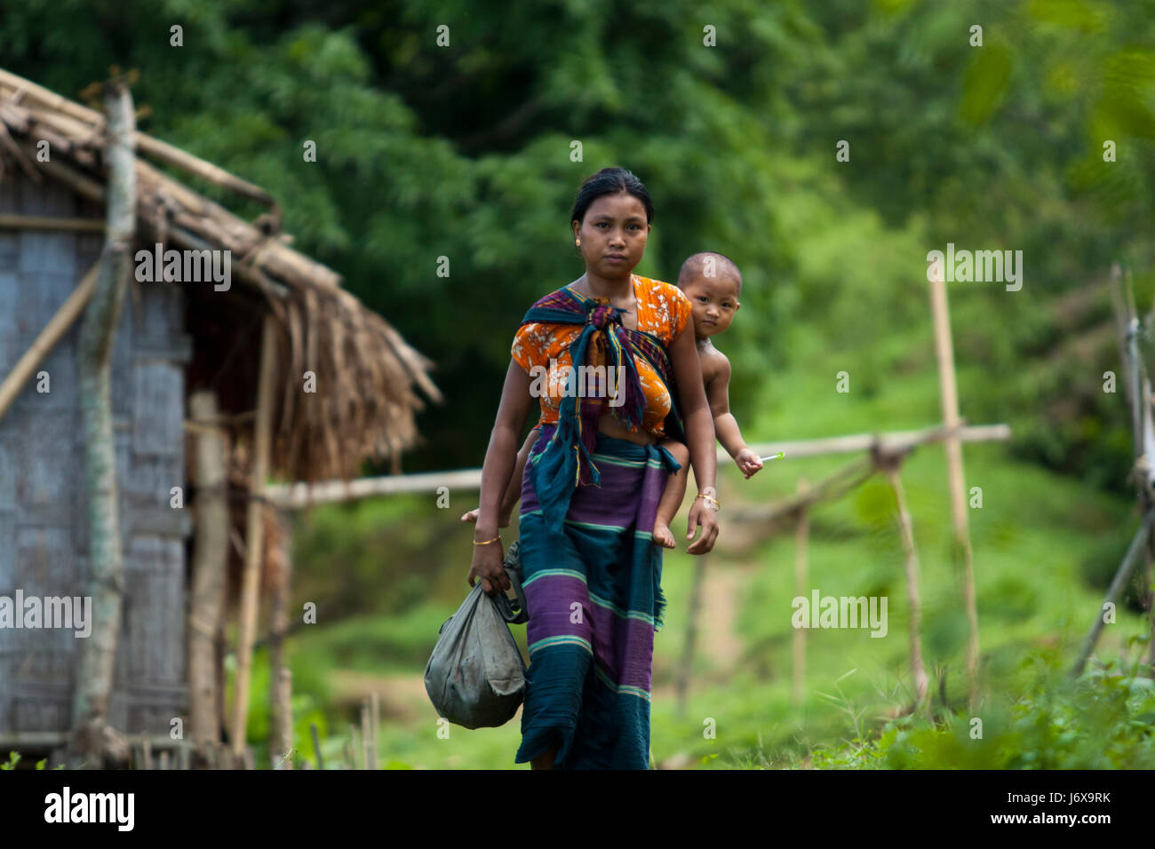 An ethnic mother carries her baby on her back. Khagrachari, Bangladesh. Stock Photo
