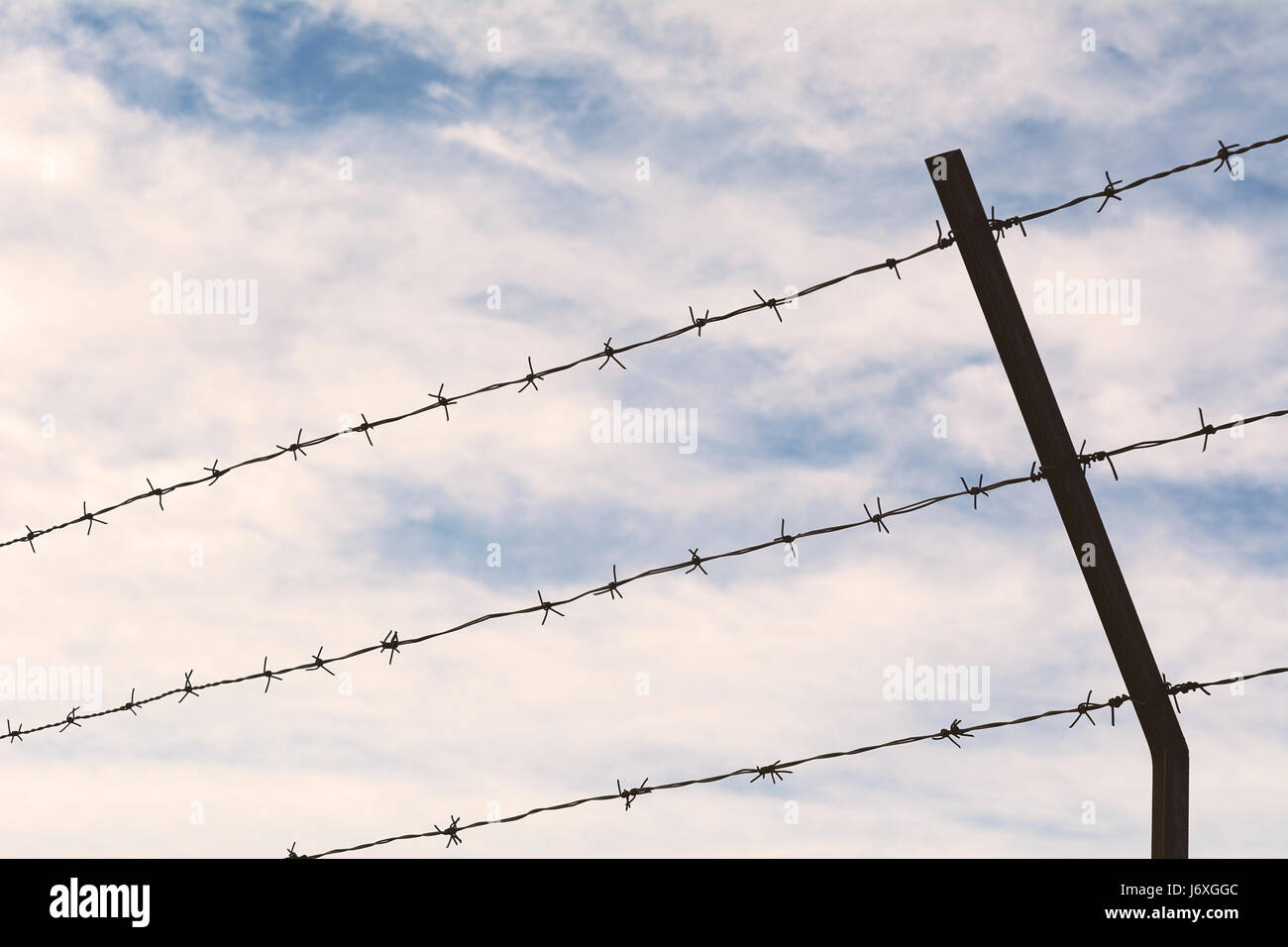 Fence of barbed wire against blue sky with clouds Stock Photo - Alamy
