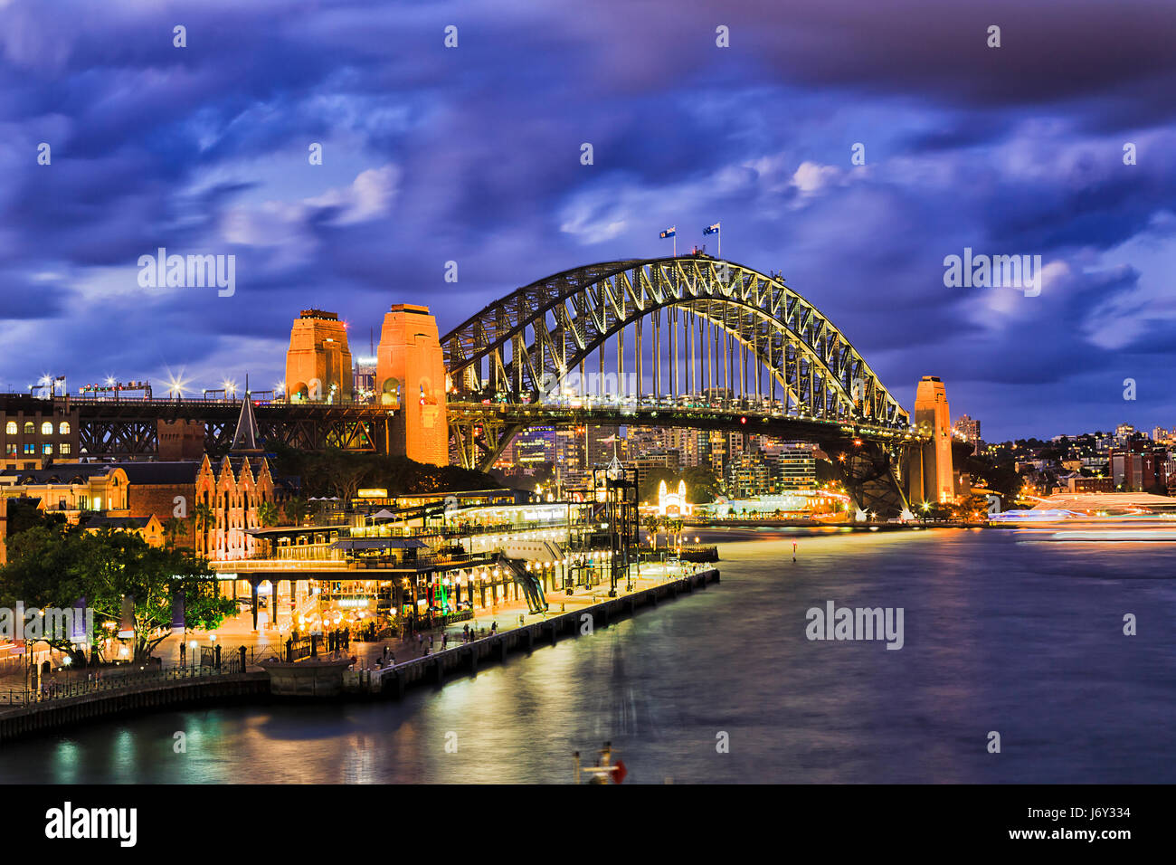 Huge illuminated arch of Sydney Harbour bridge connecting city CBD from the Rocks to North Sydney. Bright lights reflect in blurred waters of Sydney H Stock Photo