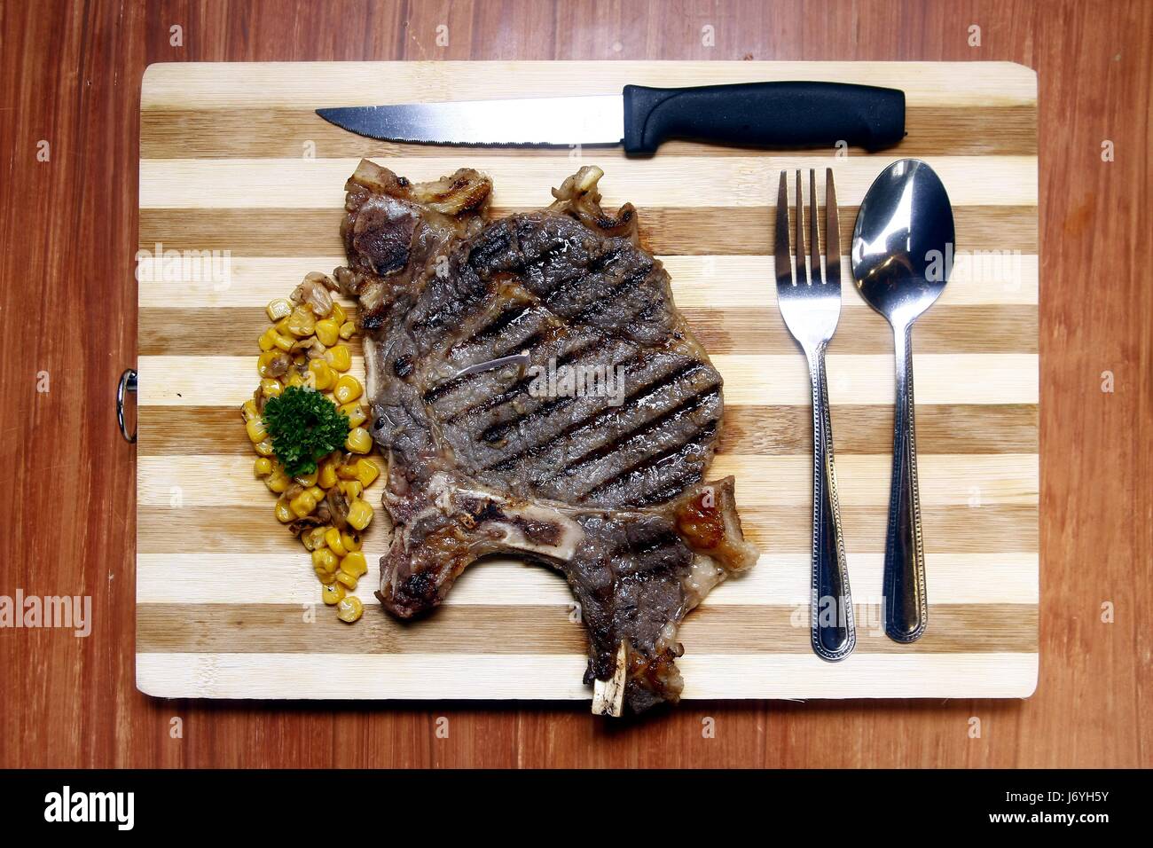 Photo of a porter house steak served on a wooden cutting board with utensils Stock Photo