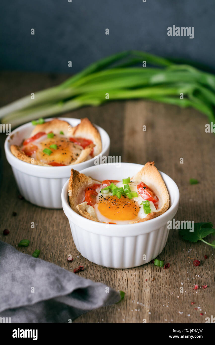 Baked eggs with tomatoes, bread and scallions Stock Photo